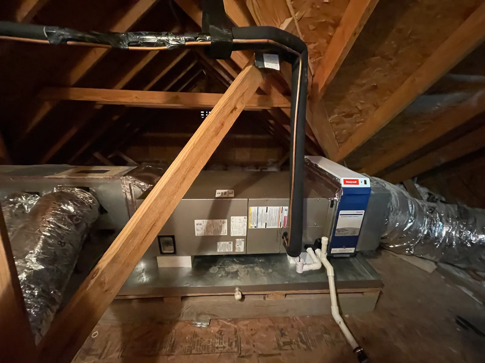 Horizontal cooling equipment in an attic with connected ducts, insulated lines and a white condensate drain.